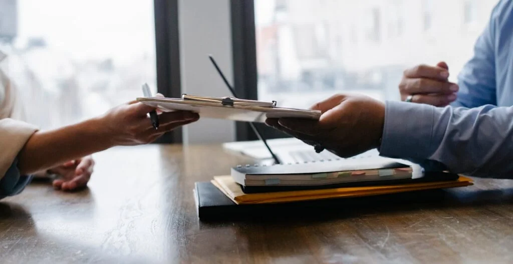 pexels-photo-5673502 Crop anonymous ethnic woman passing clipboard to office worker with laptop during job interview